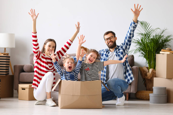 Optimistic family: man and woman raising hands near carton box with excited boy and girl while preparing to move into new apartment - Fotoğraf, Görsel