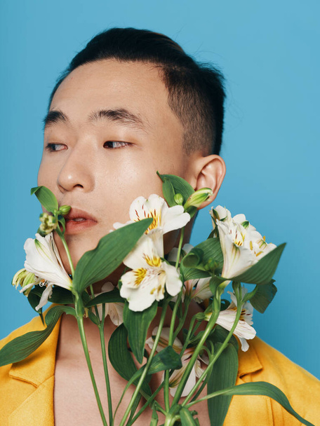 romantic asian guy with a bouquet of white flowers and in a yellow coat portrait close-up  - Photo, image