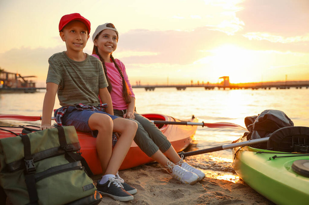 Happy children sitting on kayak near river at sunset. Summer camp - Foto, Bild