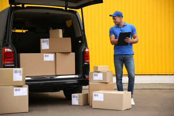 Courier with clipboard and parcels near delivery van outdoors - Foto, imagen