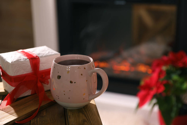 Hot drink and gift box against fireplace. Space for text - Photo, image