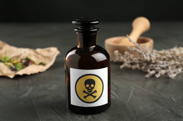 Glass bottle of poison with warning sign and herb on grey stone table - Фото, изображение