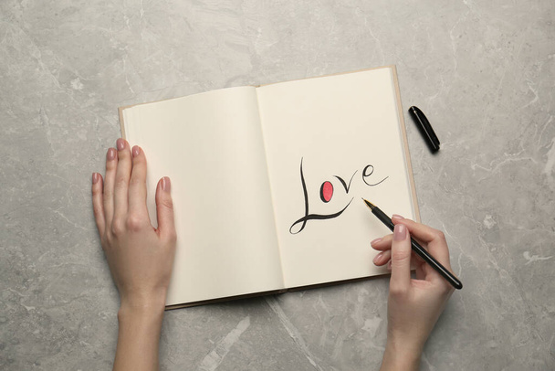 Woman writing word Love in notebook at light grey table, top view - Foto, Bild