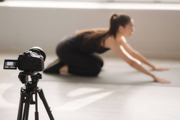 Atrakcyjna blogerka fitness nagrywa wideo na aparacie cyfrowym, dom treningowy w studio. Kobieta show pilates ćwiczenia - Zdjęcie, obraz