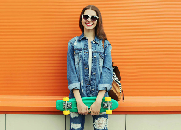 Portrait of smiling young woman with green skateboard on a colorful orange background - Foto, afbeelding