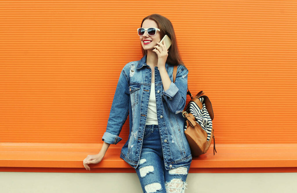 Portrait of smiling young woman calling on a smartphone wearing a denim jacket on a orange background - Foto, afbeelding