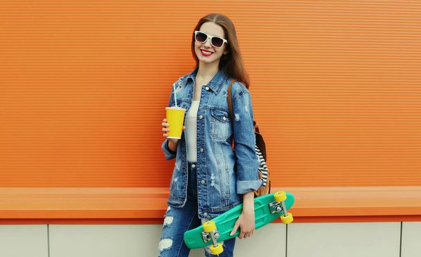 Portrait of smiling young woman with green skateboard on a colorful orange background - Fotografie, Obrázek