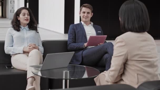 Rückansicht multiethnischer Personalchefs in Formalbekleidung, die auf schwarzen Ledersofas im Büro sitzen und unkenntliche weibliche Arbeitssuchende interviewen - Filmmaterial, Video