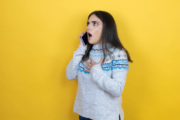 Sarı arka plan üzerine günlük süveter giyen beyaz bir kadın telefonda endişeli bir ifadeyle konuşuyor. - Fotoğraf, Görsel