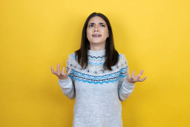Young caucasian woman wearing casual sweater over yellow background crazy and mad shouting and yelling with aggressive expression and arms raised. Frustration concept. - Fotografie, Obrázek