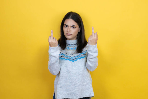 Young caucasian woman wearing casual sweater over yellow background showing middle finger doing fuck you bad expression, provocation and rude attitude. screaming excited - Photo, image