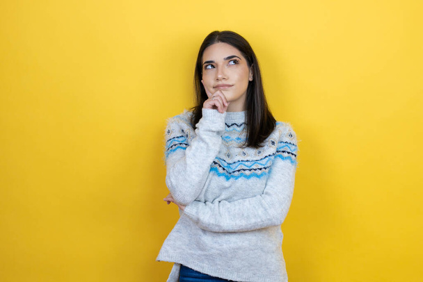 Young caucasian woman wearing casual sweater over yellow background with hand on chin thinking about question, pensive expression. smiling and thoughtful face. doubt concept. - Φωτογραφία, εικόνα