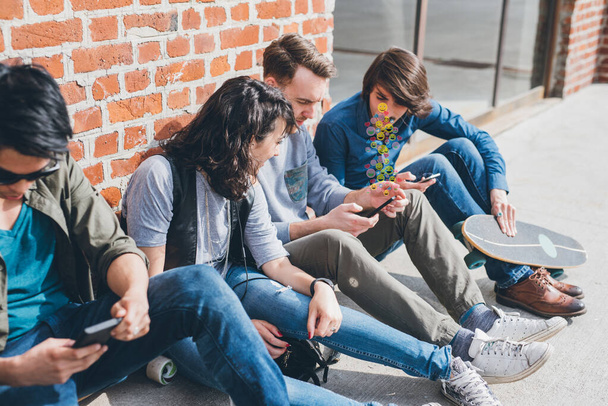 Grupo de amigos multiétnicos millennials usando teléfonos inteligentes adictos a las tendencias tecnológicas siguiendo y charlando usando emoji - Foto, imagen