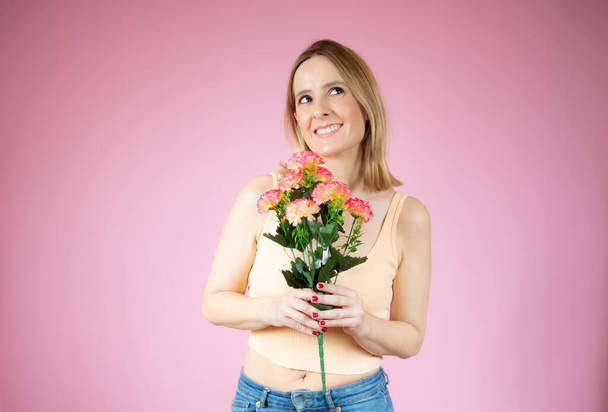 Portrait of a beautiful young woman in casual t-shirt holding big bouquet of flowers isolated over pink background - Foto, Imagem