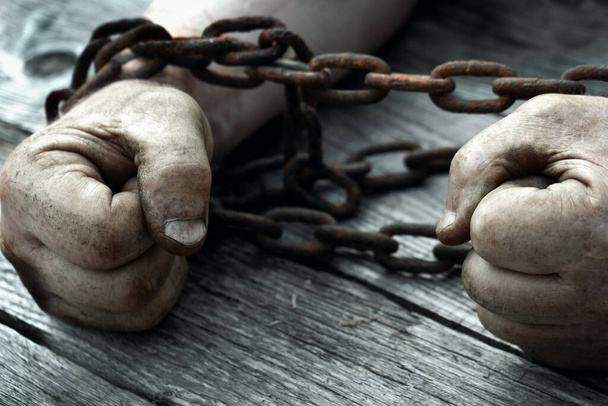 Male hands chained with old rusty chain on the wooden boards. - Foto, Imagen