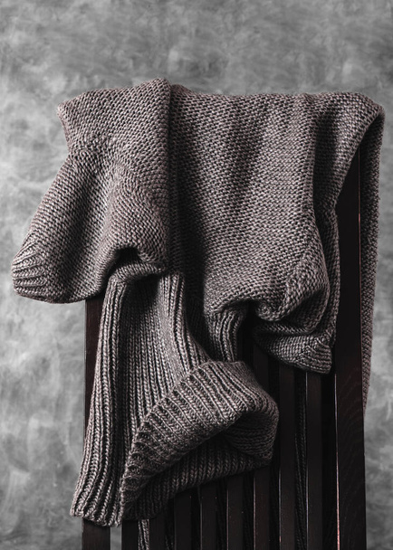 Jersey gris de punto de lana de las mujeres tirado casualmente sobre la parte posterior de la silla de madera contra la pared gris. Primer plano. Orientación vertical - Foto, Imagen