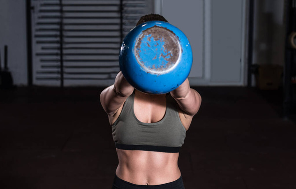 Young sweaty strong muscular fit girl holding heavy kettlebell with her hands and doing swing hardcore workout training in the gym real people exercising selective focus motion blur - Φωτογραφία, εικόνα