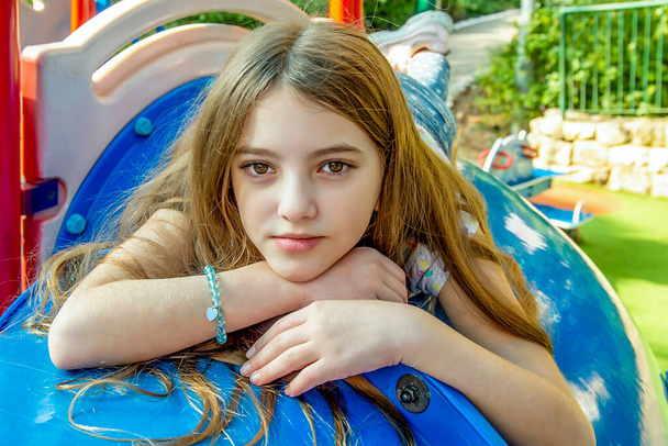 Beautiful emotional teenager girl lying on the children's city playground on a sunny day - Фото, зображення