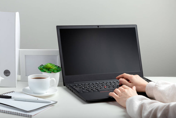 Woman works on laptop in online education on workspace. Female hands typing on laptop. Black laptop display Mock up blank. Workplace in home office for remote work minimal style on white background - Valokuva, kuva