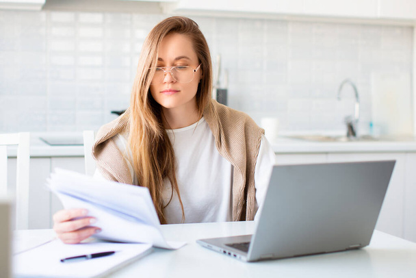 Fénykép egy nőről a laptop monitor előtt, aki papírokkal dolgozik. - Fotó, kép