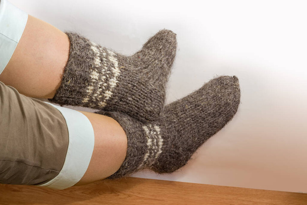 Paire de chaussettes épaisses en laine grise tricotées à la main sur les jambes des femmes contre le sol en bois et le mur léger - Photo, image