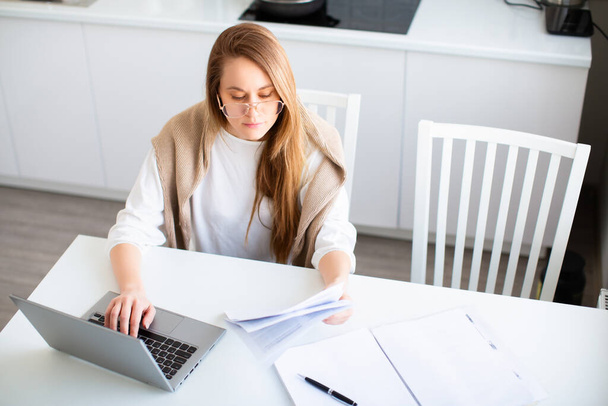 Online munkaterv. A nő online dolgozik egy laptop monitor előtt. Adónyomtatványokat tölt ki, vagy számlákat fizet. Fénykép otthon belső. - Fotó, kép