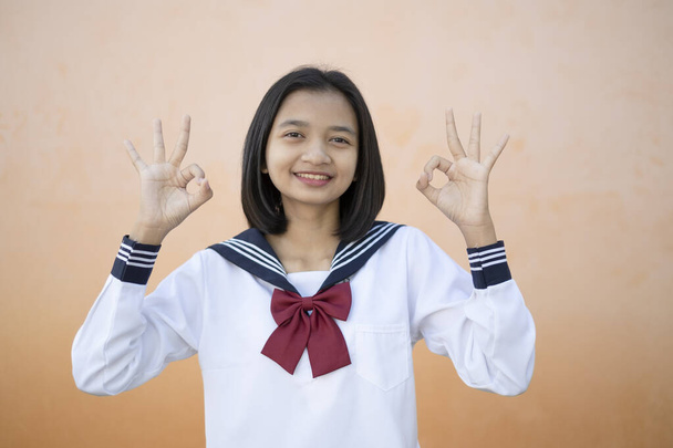 Portret szczęśliwy młoda dziewczyna nosi mundur w szkołach.Orange tle. - Zdjęcie, obraz