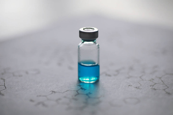 kleine potjes met injectie en injectiespuit voor injectie op blauwe achtergrond in de buurt van de chemische vorm - Foto, afbeelding