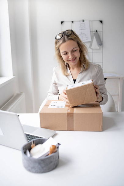 блондинка бизнес-женщина сидит в своем офисе и только что получил несколько пакетов, подарков, доставка из онлайн-заказа и счастлив - Фото, изображение