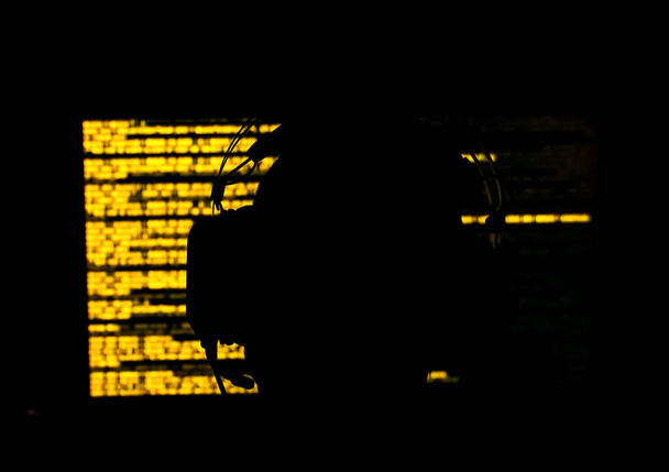 Silhouette eines Hackers, der in einem dunklen Raum vor einem Monitor mit gelbem Code sitzt. Geringe Schärfentiefe. Hochwertiges Foto - Foto, Bild