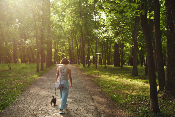 Junge Frau geht mit kleinem Hund Yorkshire Terrier im Park spazieren - Foto, Bild