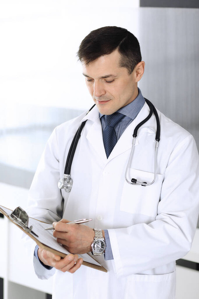 Doctor man using clipboard for filling up medication history records. Perfect medical service in clinic. Physician at work in hospital. Medicine and healthcare concepts - Fotoğraf, Görsel