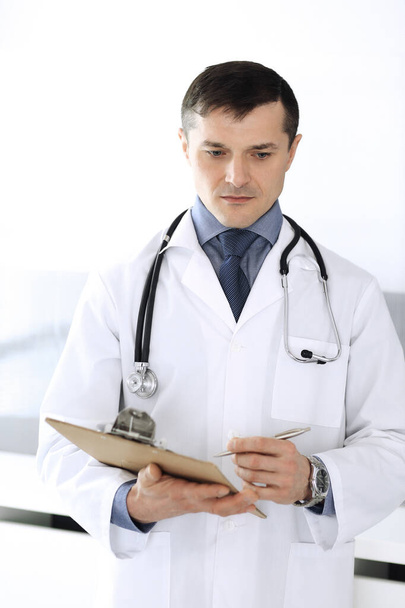 Doctor man using clipboard for filling up medication history records. Perfect medical service in clinic. Physician at work in hospital. Medicine and healthcare concepts - Photo, Image