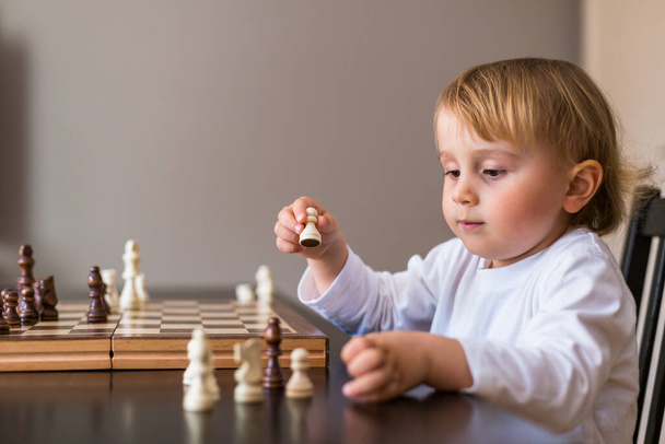 Kleine Jungen lernen Schach. Das Kind sitzt zu Hause am Tisch neben dem Schachbrett. Schachfrüherziehung. - Foto, Bild