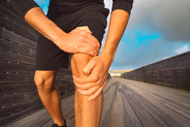 Hombre corredor sosteniendo su rodilla dolorosa debido a una lesión. Lesión por entrenamiento y ejercicio - Foto, imagen