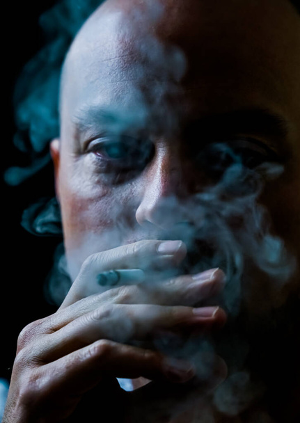 Man smoking a cigarette blowing out white smoke. Isolated on black background, shallow depth of field. High quality photo - Photo, Image