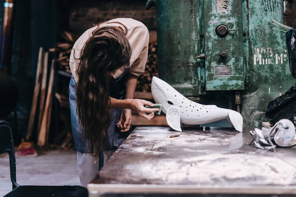 Portrait of young woman carefully work on a ceramic whale in workshop. - Zdjęcie, obraz