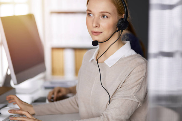 Businesswoman talking by headset while sitting in sunny office. Call center and diverse people group in business - Foto, Imagem