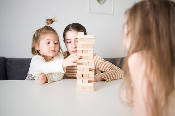 children play board game jenga. girls build tower of wooden blocks, concept of developing fine motor skills, home joint games. Leisure activities for children at home. - 写真・画像