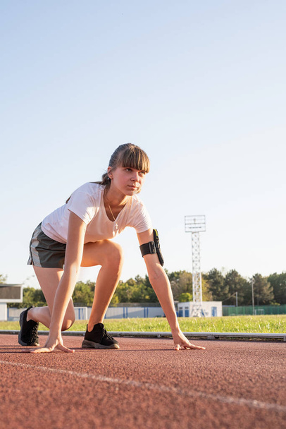 Sports et fitness. Adolescente se prépare à courir sur la piste du stade - Photo, image