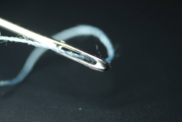 Macro fotografía de aguja de coser. Aguja pequeña con hilo en el ojal, aislada sobre el fondo negro. - Foto, Imagen