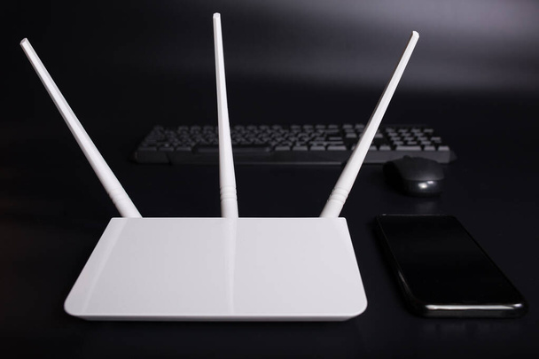 Biały router wifi z trzema antenami ze smartfonem i klawiaturą PC na czarnym tle. - Zdjęcie, obraz