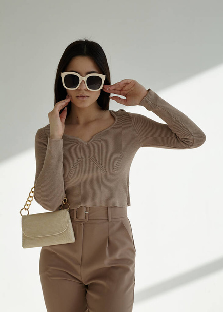 portrait of a beautiful brunette in a stylish spring suit with glasses and a bag - Foto, Imagen