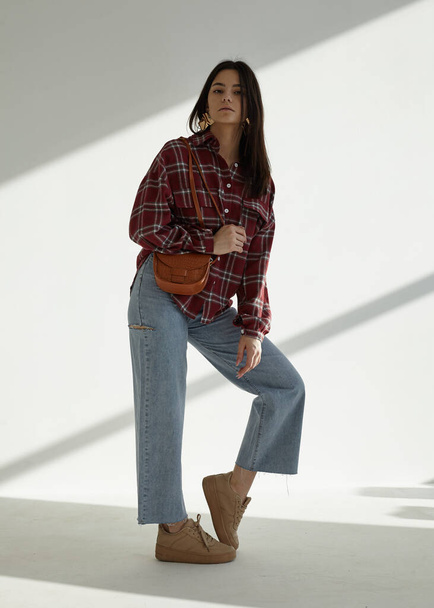 beautiful brunette in jeans and a red plaid shirt with a bag in her hands  - Foto, Bild