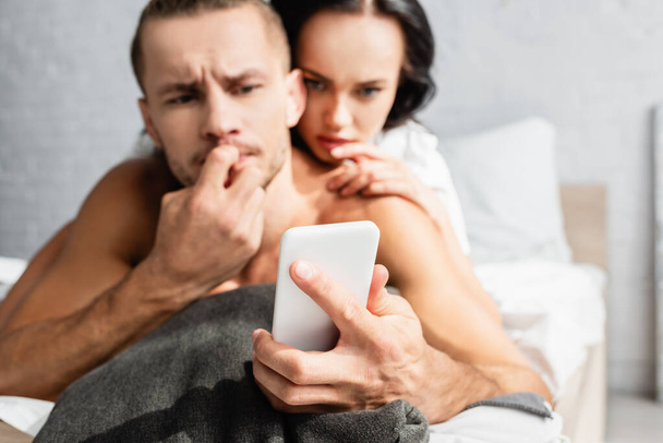 Smartphone v ruce zamyšlený muž a přítelkyně na rozmazaném pozadí  - Fotografie, Obrázek