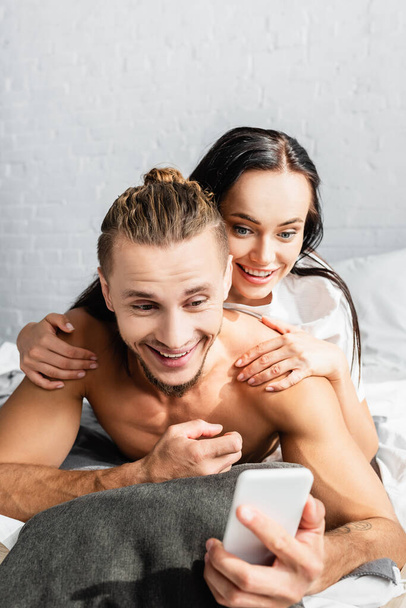Homem alegre usando smartphone perto da namorada no quarto  - Foto, Imagem