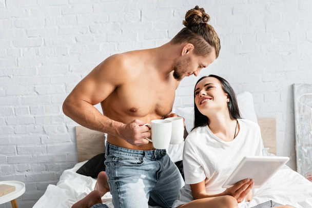 Shirtless man with cups standing near smiling woman with digital tablet  - Fotoğraf, Görsel
