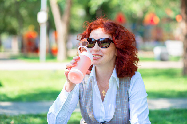 Молода жінка на відкритому повітрі в парку п'є воду з багаторазової пляшки. Зменшення пластику
 - Фото, зображення