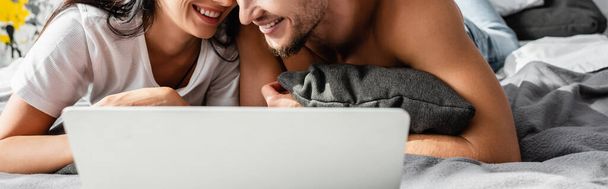 Gestroopt uitzicht van glimlachend paar liggen in de buurt laptop op bed, banner  - Foto, afbeelding