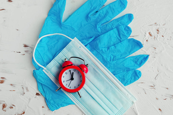 Face mask, medical gloves and alarm clock on the table. Coronavirus concept - Photo, Image